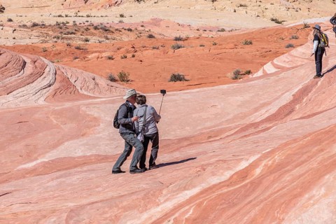 Couple use selfy stick for picture on a layered sandstone rock formation in the Fire Wave area of