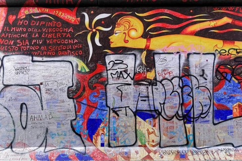 Colourful mural with a fiery female figure and Italian lettering, overlaid with large graffiti