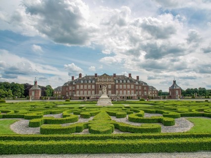 Large historic castle with manicured hedges forming a labyrinth under a cloudy sky, old red brick