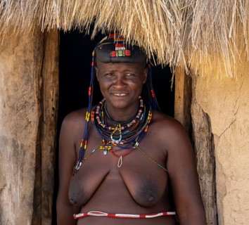Hakaona woman with traditional kapapo hairstyle, in the entrance of her mud hut, portrait, in the