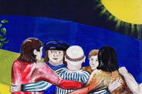 Mural shows a group of people hugging each other under a deep blue sky and a bright sun, Wall