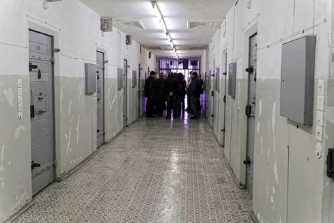 Group of people in the corridor of a prison with grey doors and neon lighting,