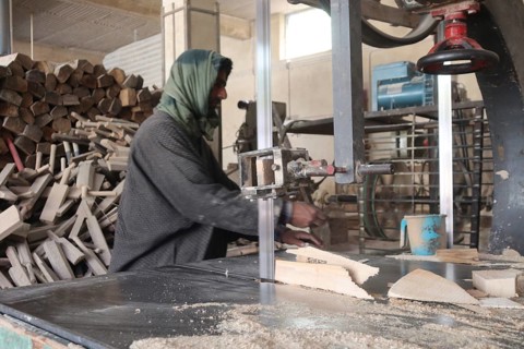 Man working in a wood workshop with machinery and logs around, wearing traditional clothing,