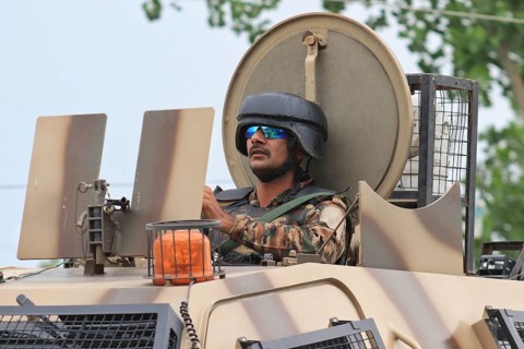 A soldier in an armored vehicle wearing a helmet and sunglasses, leaving encounter site in Pulwama,