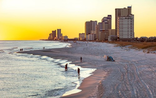 People walking and playing on the beach as the sun sets over the Gulf of Mexico at Gulf Shores,