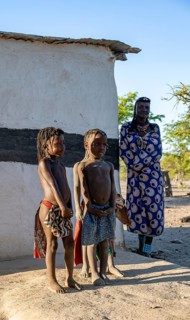 Hakaona woman and two traditional Hakaona children in front of their mud hut, in the morning light,