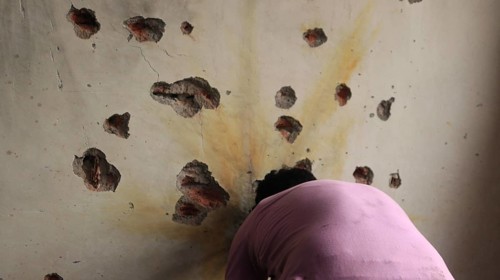 A man facing a wall riddled with bullet holes, sign of destruction in an indoor setting, Encounter,