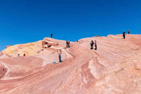 Hikers on layered sandstone rock formations in the Fire Wave area of Valley of Fire State Park near