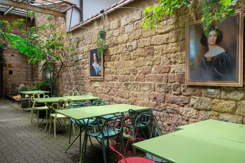 A picturesque garden area of a cafe with green tables and chairs, decorated with portraits on the