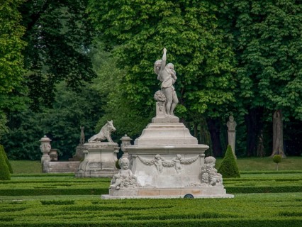 Elegant stone figure in a lush, well-kept garden surrounded by green trees and hedges, old red