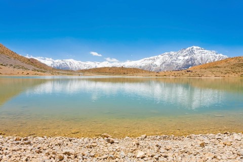 A pristine alpine lake reflects the surrounding Himalayan mountains. The lake is a pilgrimage point