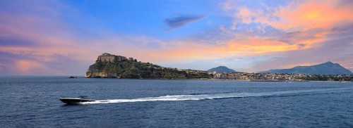 Italy, scenic sunset over Procida Island near Naples with boat approaching it from afar, Europe