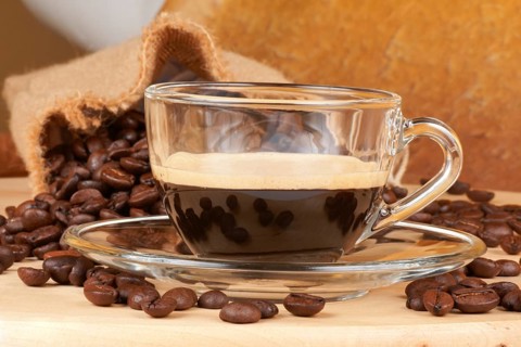 Close-up of a glass cup with italian espresso over a wooden table, surrounded by coffee beans