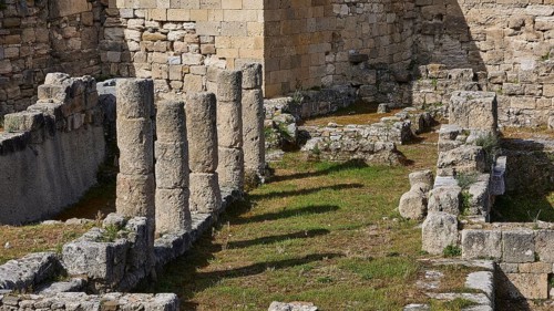 Close-up of ancient stone columns and walls overgrown with grass, part of an archaeological site,