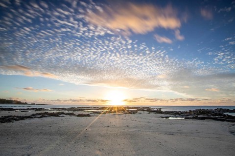 Sunrise over the sea with gentle waves. Sandy beach with lava rocks and blue water alternating with
