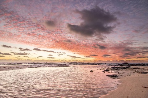 Sunrise over the sea with gentle waves. Sandy beach with lava rocks and blue water alternating with