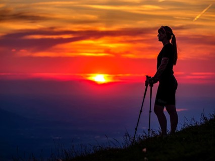 Silhouette of a young slender woman with hiking poles on a mountain meadow at sunset, Schlenken,