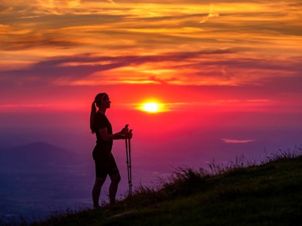 Silhouette of a young slender woman with hiking poles on a mountain meadow at sunset, Schlenken,