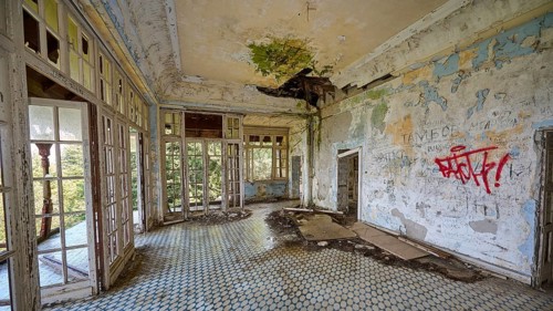 Abandoned room with broken roof, graffiti on the walls and light coming in through the windows,
