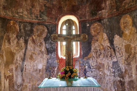 Altar with a cross and flowers in front of an artistically painted wall in an old church, chancel,