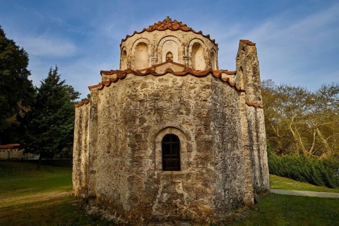 Old stone church in the middle of a forest, with red tiled roof and blue sky in the background,