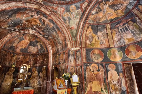 A church interior with dark frescoes on the walls, decorated with religious art and altars,