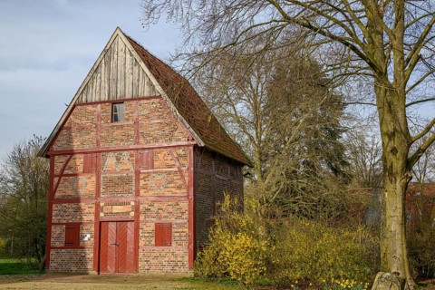 Half-timbered house with red wooden doors and flowering bushes in front of a tree, Vreden, North