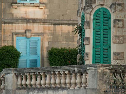 Close-up view of a building with green shutters, balcony railings and landscaped garden, valetta,