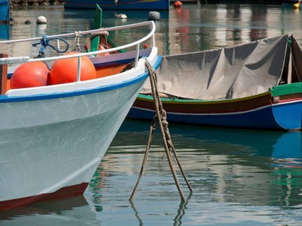 A quiet harbour with anchored boats floating on the reflecting water, marsaxlokk, mediterranean