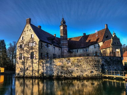 Medieval castle with moat and large tower, which stands out due to a reflection in the water,