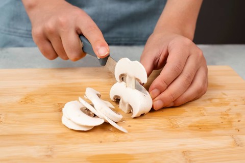Cutting champignon mushrooms on a wooden board, prepare salad, healthy food with vegetables, fresh