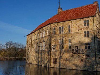 Close-up of a historic stone building with a red tiled roof reflected in the water, lüdinghausen,