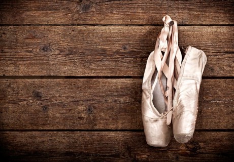 Old used pink ballet shoes hanging on wooden background