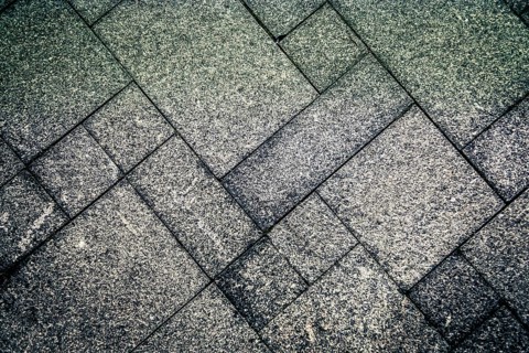 Gray concrete tiles arranged in a geometric pattern creating a rough and textured surface,