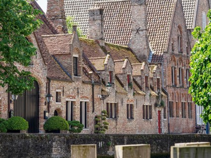 Historic brick building with decorative gables and green tree in sunny weather, Bruges, Flanders,