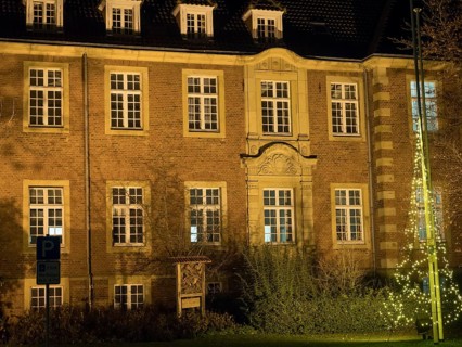 A historic building with illuminated windows at night. The warm light emphasises the details of the