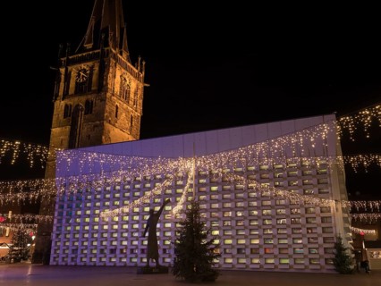 Illuminated Christmas market decoration at night with lights and a large tower in the background,