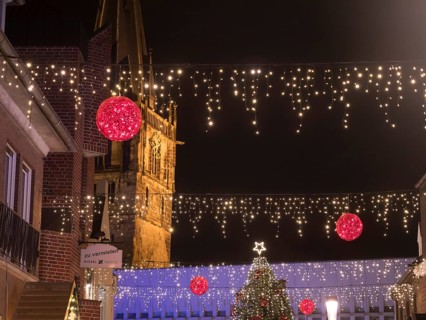 Night shot of an alley decorated for Christmas with fairy lights and a church in the background,