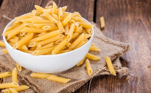 Uncooked Penne (detailed close-up shot) on rustic wooden background