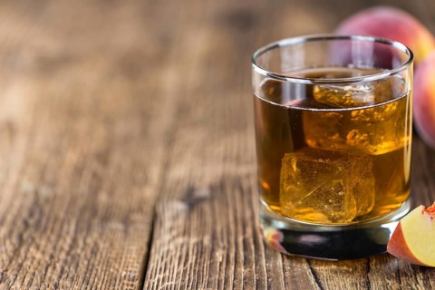 Fresh made peach ice tea (selective focus) on an old wooden table (close-up shot)