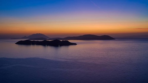 A calm sunset over the sea, the islands in the background surrounded by a gentle colour gradient of