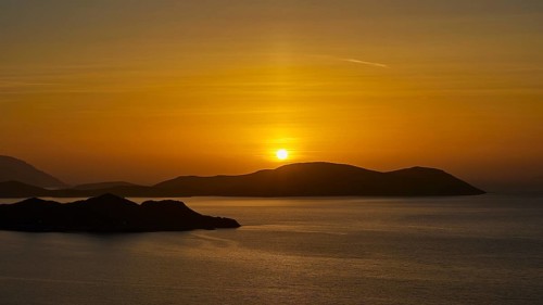 A sunset over the sea, bathing the sky in golden colours and showing tranquil islands in the