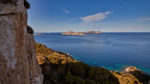 View from a cliff to the open sea and several islands in the distance under a blue sky, Makri