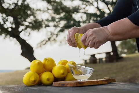 Woman squeezes a lemon with her hands the juice falls into a glass bowl, in the background is a