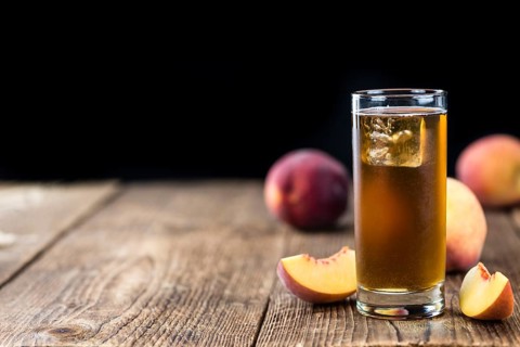 Old wooden table with fresh made tasty peach ice tea (selective focus)