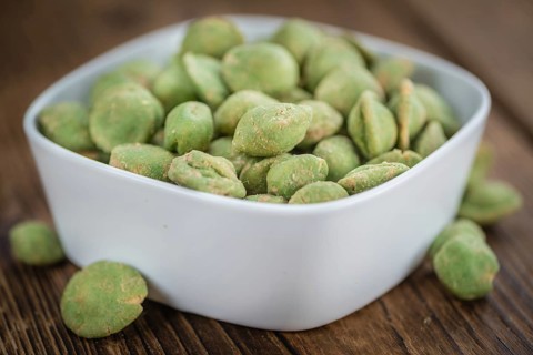 Wasabi coated Peanuts as high detailed close-up shot on a vintage wooden table (selective focus)