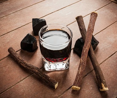 Licorice liqueur with pure blocks and roots on wooden table