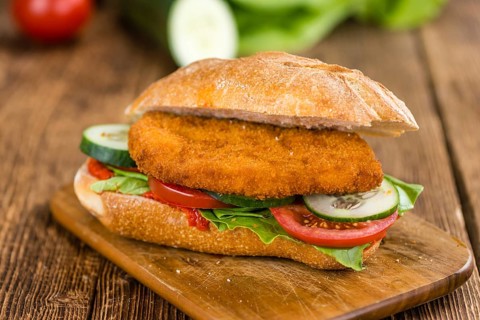 Bun with a Chicken Schnitzel on wooden background (close-up shot, selective focus)