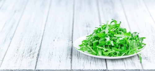 Wooden table with fresh Arugula as detailed close-up shot (selective focus)