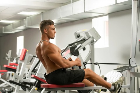 At gym. Photo of sexy young man trains on simulator